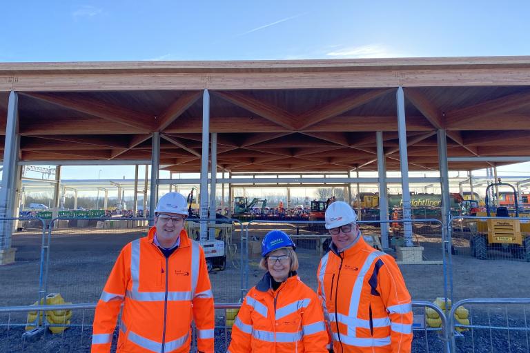 Councillors Tom Cunningham, Lesley Wagland and Kevin Bentley in hardhats and hi-vis in front of the station building construction.