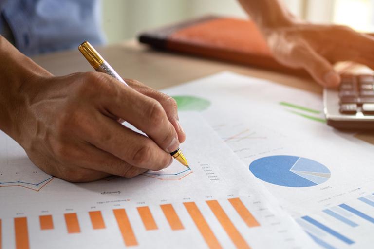 Close up of hand writing on a piece of paper with charts on them