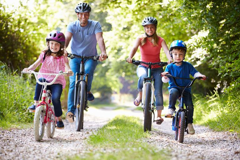 A dad, daughter, son and mum on bicycles wearing helmets cycling through some woodland.