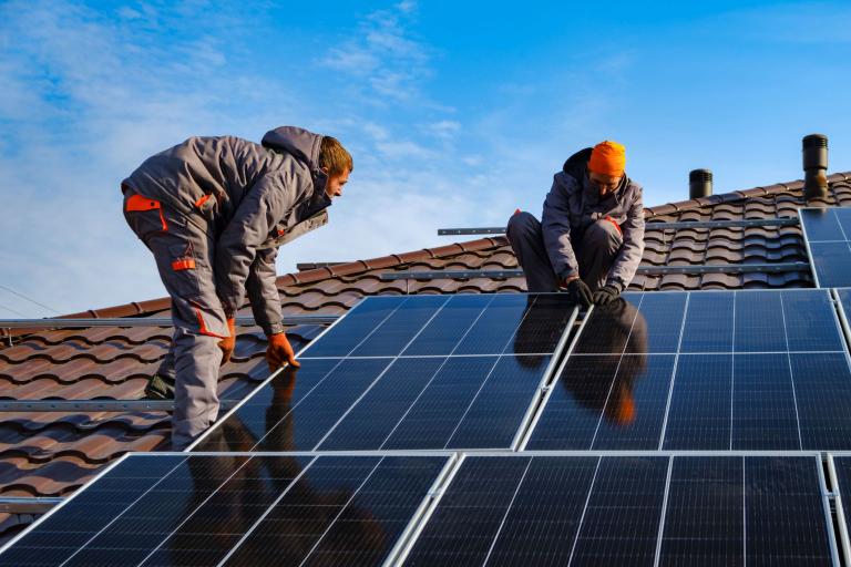 Two men working to fit some solar panels to a roof.