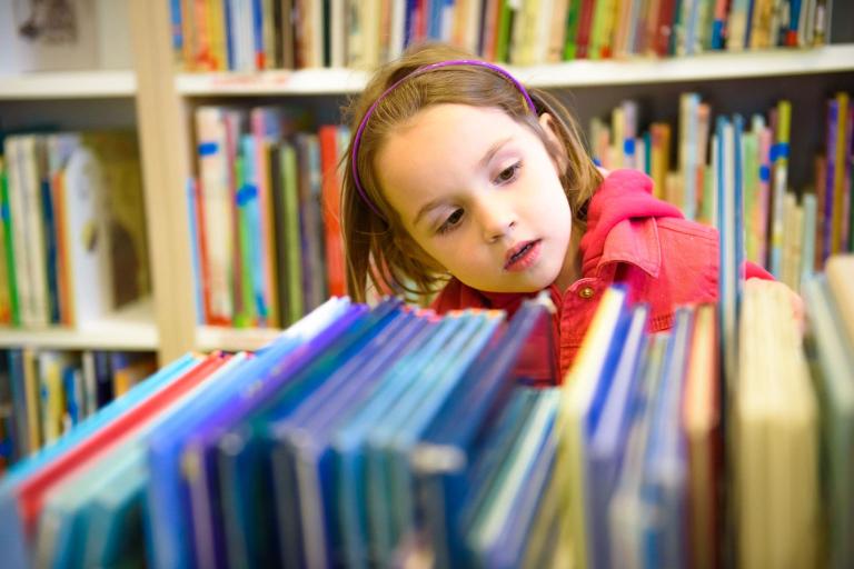 A young girl browsing some books on a library shelf.