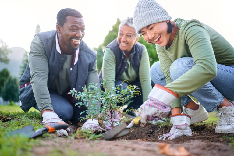three people smiling while volunteering in a park planting a tree
