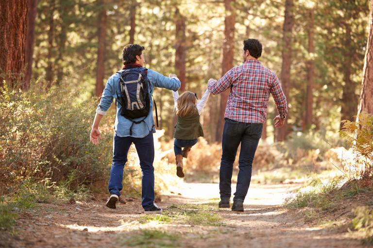 Two men walking in a forest holding hands with a young girl