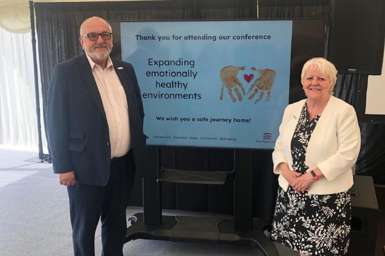 Councillor Tony Ball, Cabinet Member for Education Excellence, Lifelong Learning and Employability, and Councillor Beverley Egan, Cabinet Member for 	Children’s Services and Early Years, standing in front of a TV screen at the Emotional Wellbeing and Mental Health Conference