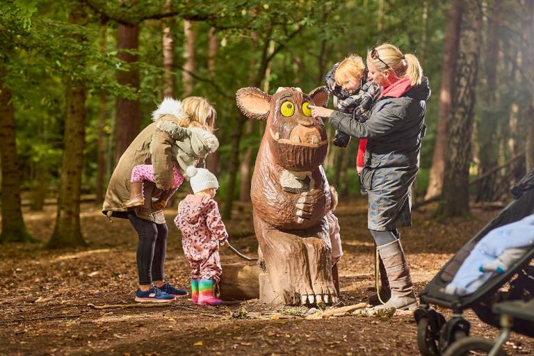 Two women and three young children looking at a Gruffalo sculpture inside the woodland at Thorndon Country Park