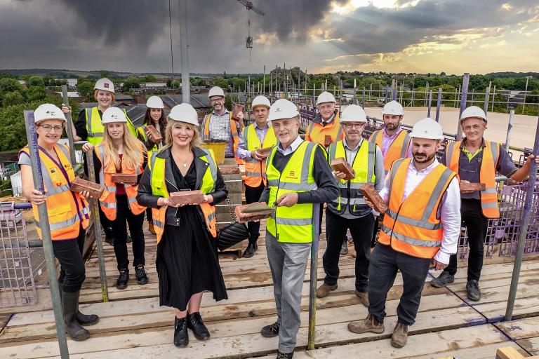 A group of people in yellow and orange high-visibility clothing holding bricks at the Shernbroke site