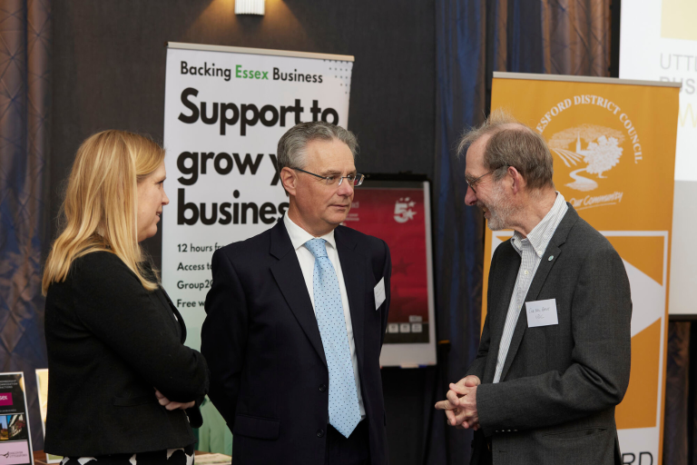 A woman and two men chatting at an event, standing in front of some banners.