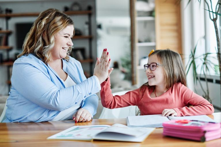 A woman and child high five in front of a table of school books
