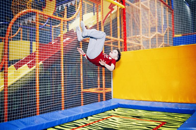 A young boy bounces on a trampoline in a soft play centre.