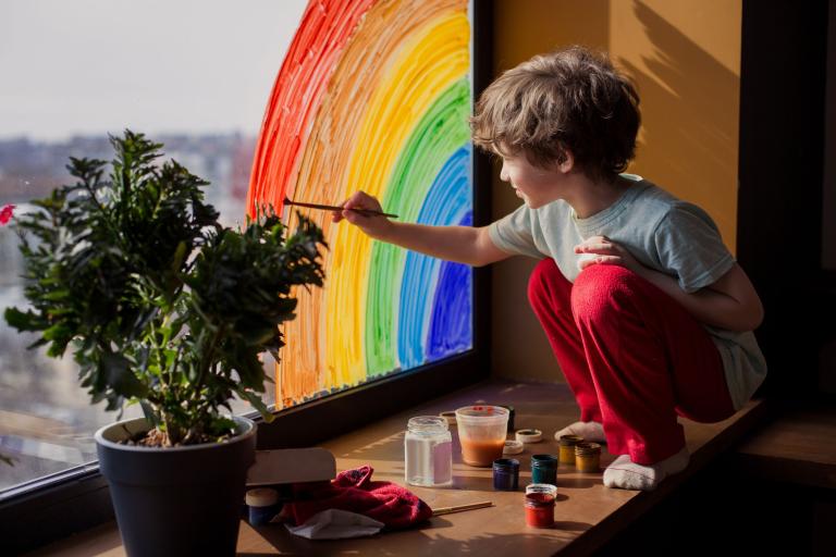 A boy at home paints a rainbow on the window
