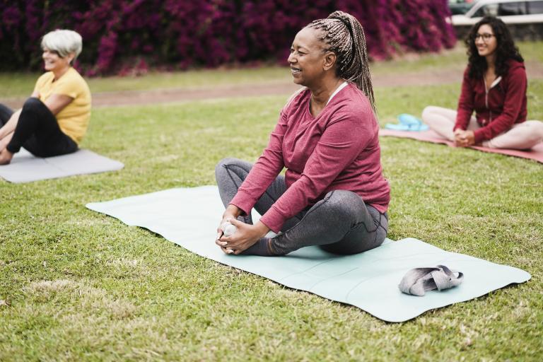 Three women sitting on yoga mats outside on an area of grass. 