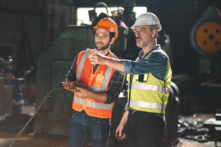 Two men dressed in high-visibility clothing and hard hats in a engineering workplace.