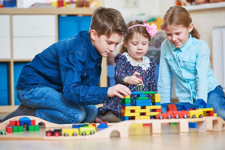 A boy and two girls playing with a brick train set.