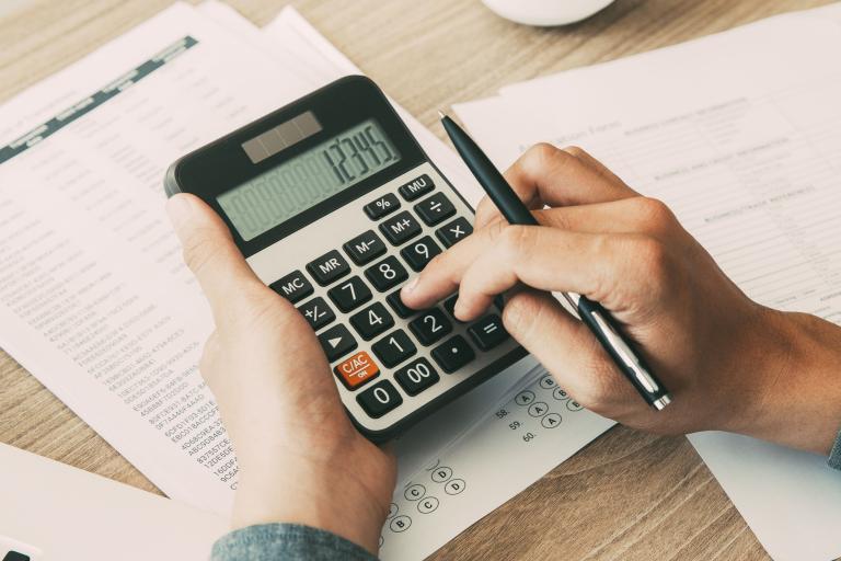 A man's hands holding a calculator and a pen, above notebooks.