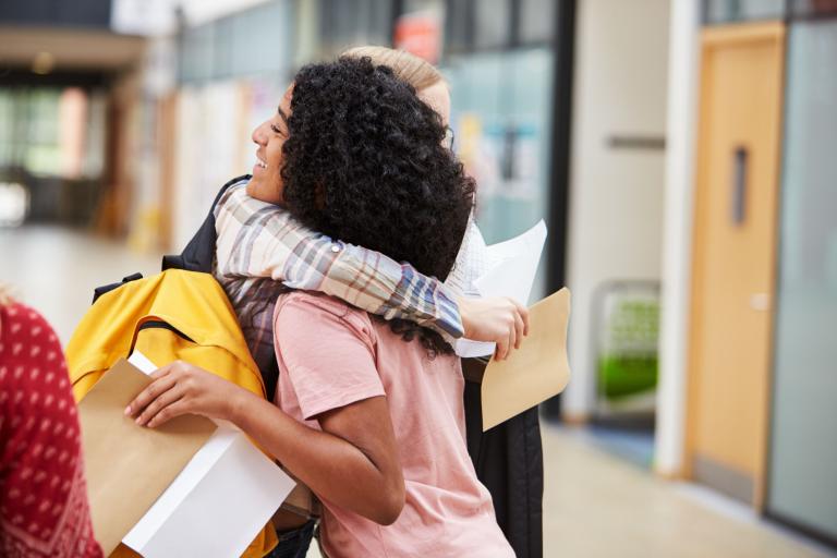Two female students hugging while holding exam results.