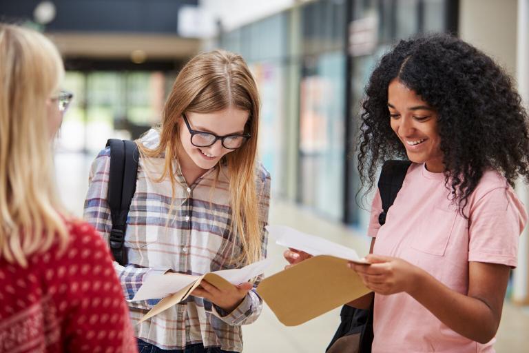 A group of teenage girls opening envelopes to see their exam results. They are smiling.