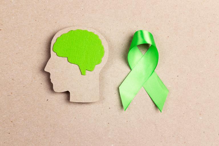 Cardboard cut-out of a head's side profile with a green ribbon laid to its left.