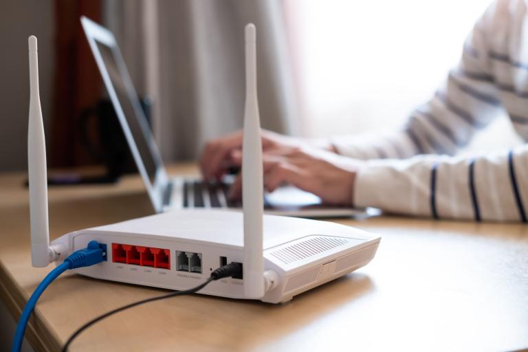 A close up of a broadband router, with a person working at a laptop behind.