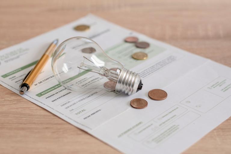 A lightbulb, pen and pennies sitting on top of an energy bill. 