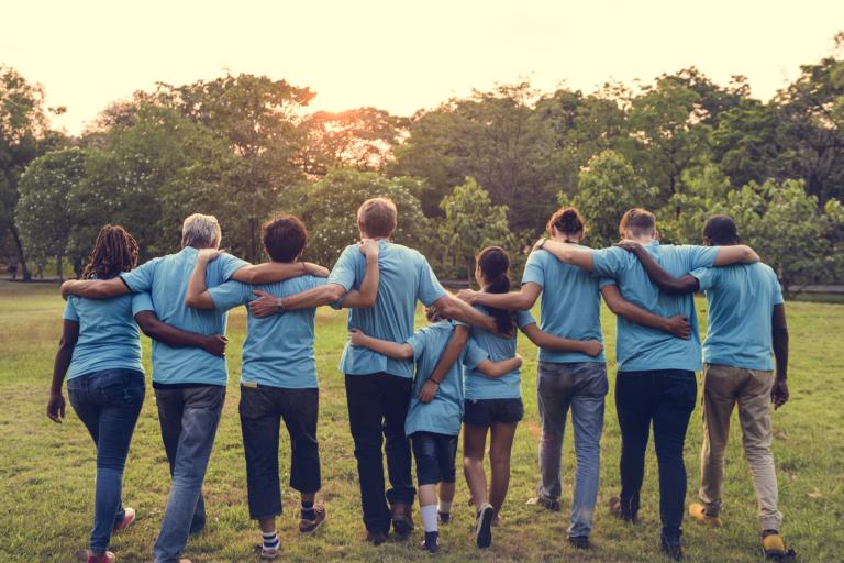 A group picture from behind of a group of people with their arms interlocked walking through a field..