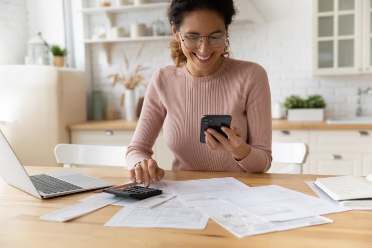 smiling woman at a desk with a phone, calculator and laptop