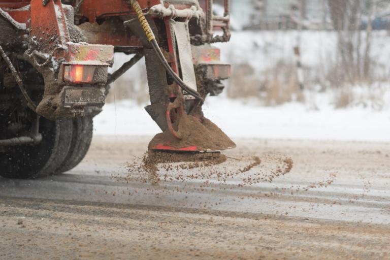 A close up of a gritter spreading salt on a snowy road.