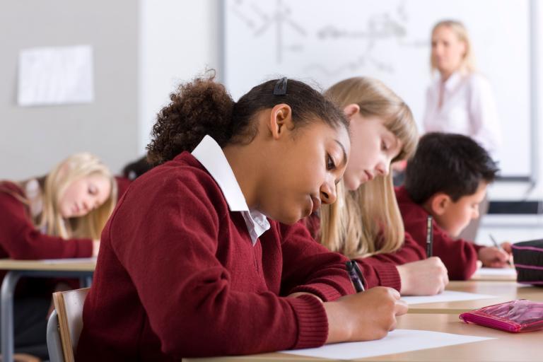 A group of schoolchildren wearing burgundy school jumpers writing at desks