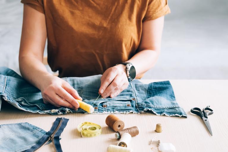 A woman with a collection of sewing tools working on a piece of denim.