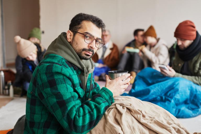 A man in a sleeping bag holding a cup of coffee.