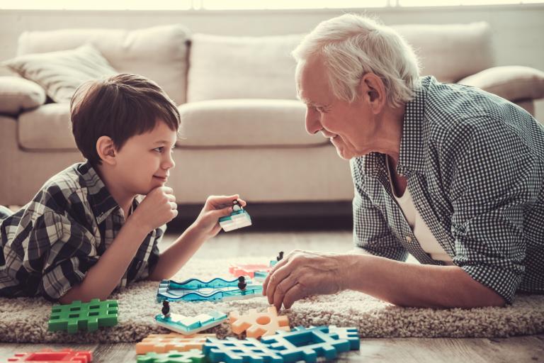 A young boy and an elderly man on laying on the floor playing with some toys