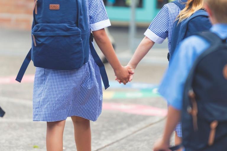 Two primary schoolgirls hold hands in a playground.