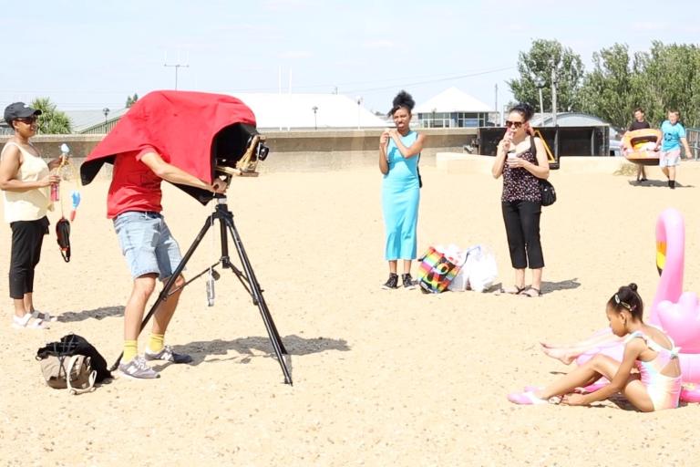 Videographer films family on beach using old-fashioned camera.