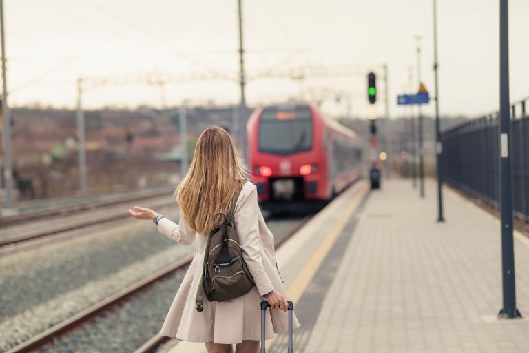 A woman with a pull along suitcase facing towards a train pulling in at a station.