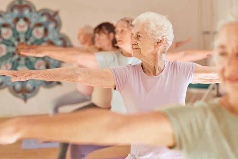 A group of elderly women standing in a row in a yoga pose.