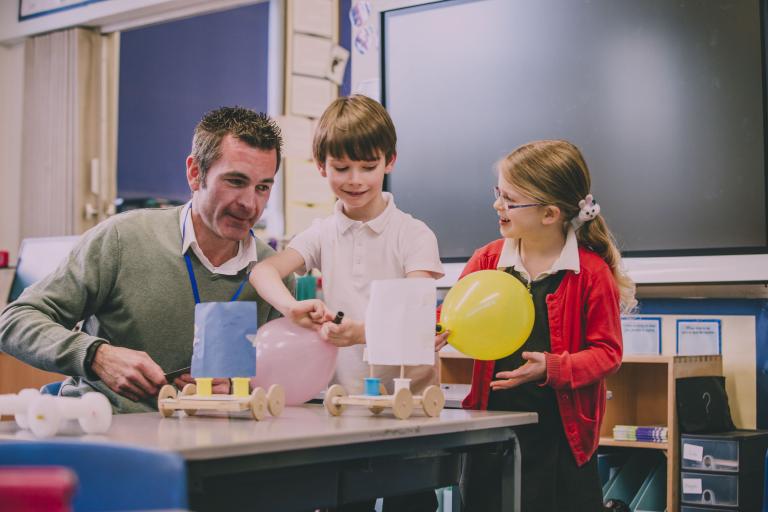 A male teaching assistant doing some crafts with a young boy and girl.