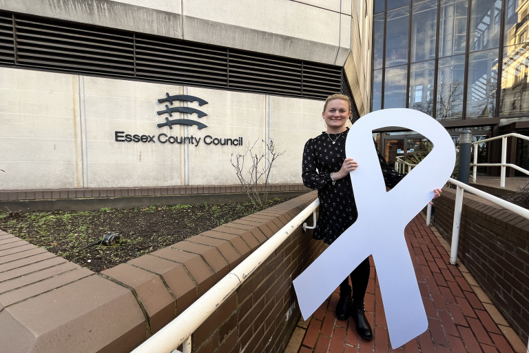 Councillor Louise McKinlay stands on the steps of county hall. He is holding a giant white ribbon.