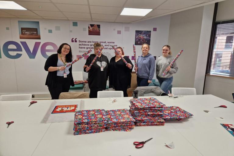 A group of smiling employees holding up rolls of wrapping paper and cheering