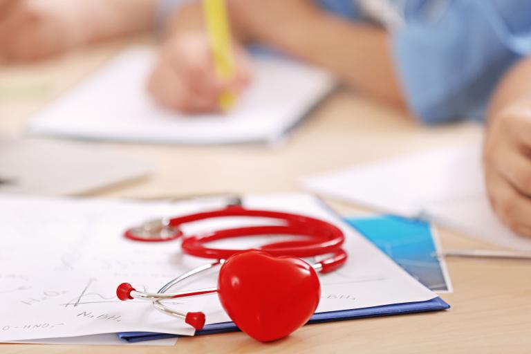 A close up of a red stethoscope sitting on a desk with papers.