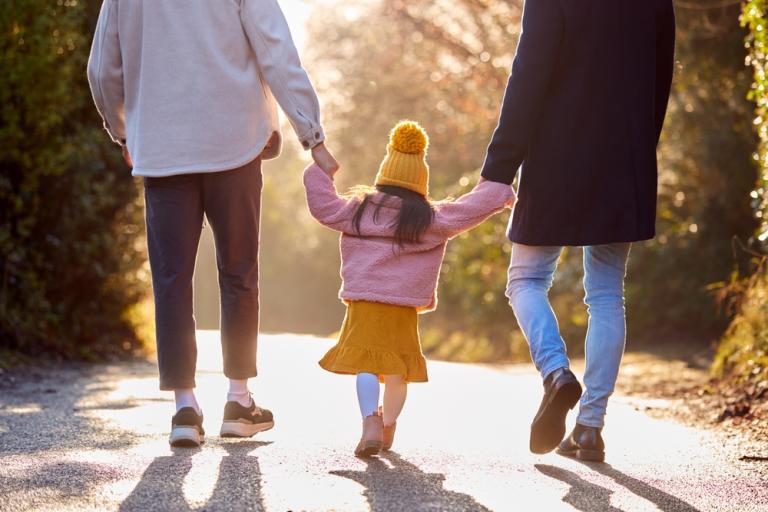 rear view of two dads walking with girl child in autumn countryside