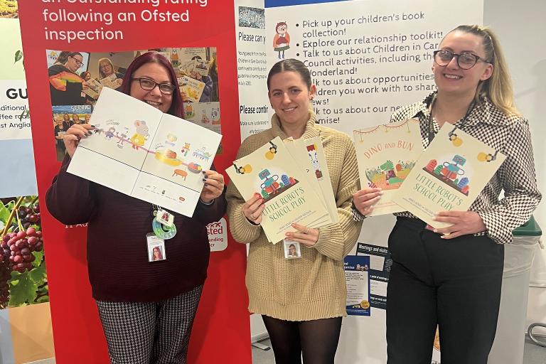 Three women holding up copies of the symbol versions of the children's books.