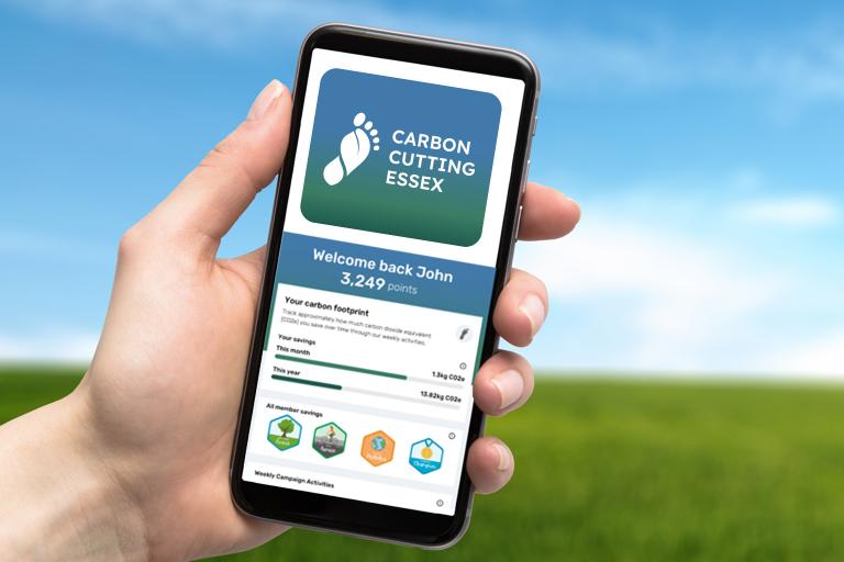 A hand holding a phone displaying an image from a screen of the Carbon Cutting Essex app.