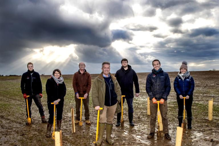 Cllr Peter Schwier flanked by Essex County Council employees with shovels in a wet field.