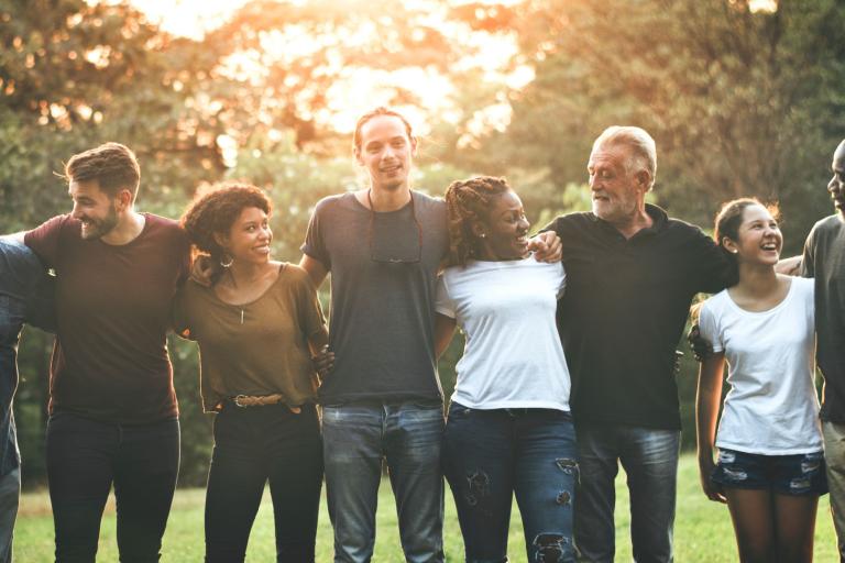 A group of people gathered outside smiling, with arms around each other.