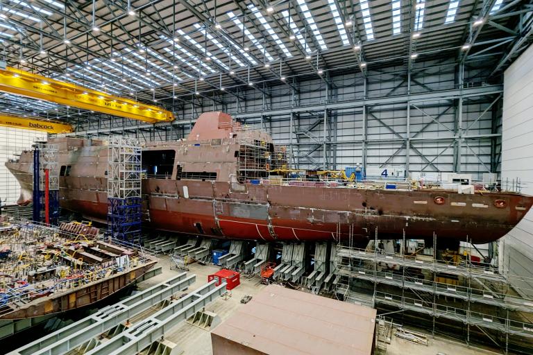 Half-built Royal Navy frigate suspended on hydraulic jacks during construction.