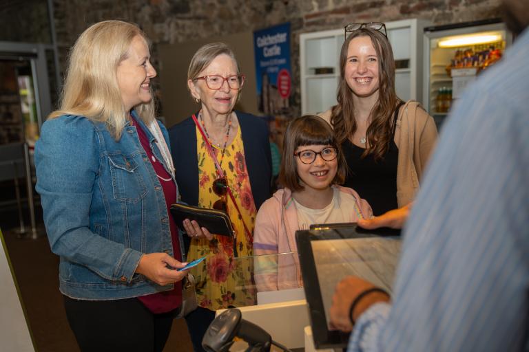 Four people of various ages smiling as the stand at a cash register