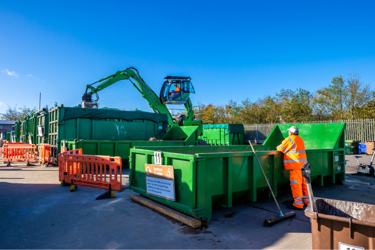 A site worker in front of a green container at a recycling centre with a blue sky