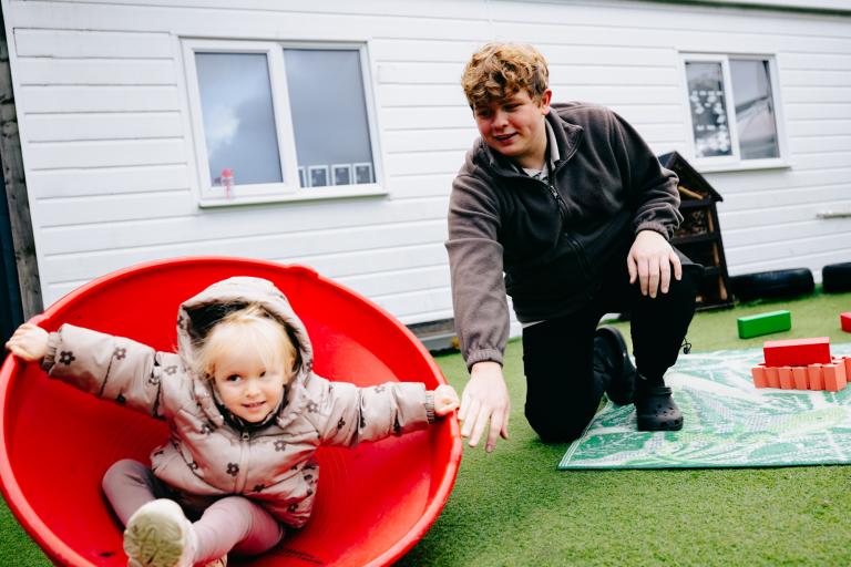 Male early years practitioner with a young girl playing outside