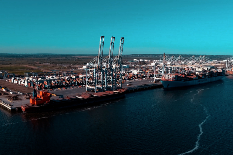 An overhead shot of a port, showing a number of shipping containers and mechanical equipment such as cranes.
