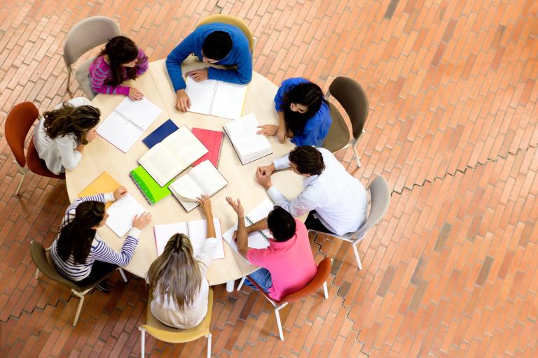 Aerial view of a group of adults huddled around a circular table working on a project.