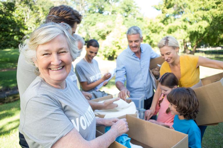 A group of smiling volunteers. They are standing in a sunny, wooded area.